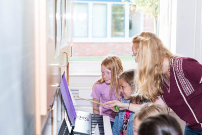 Die Lehrerin zeigt den Schülerinnen und Schüler wie man Noten für das Klavierspiel liest